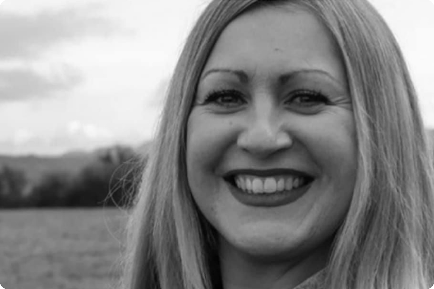 Black and white close up photo of Carolyn smiling at the camera. She has long blonde hair.