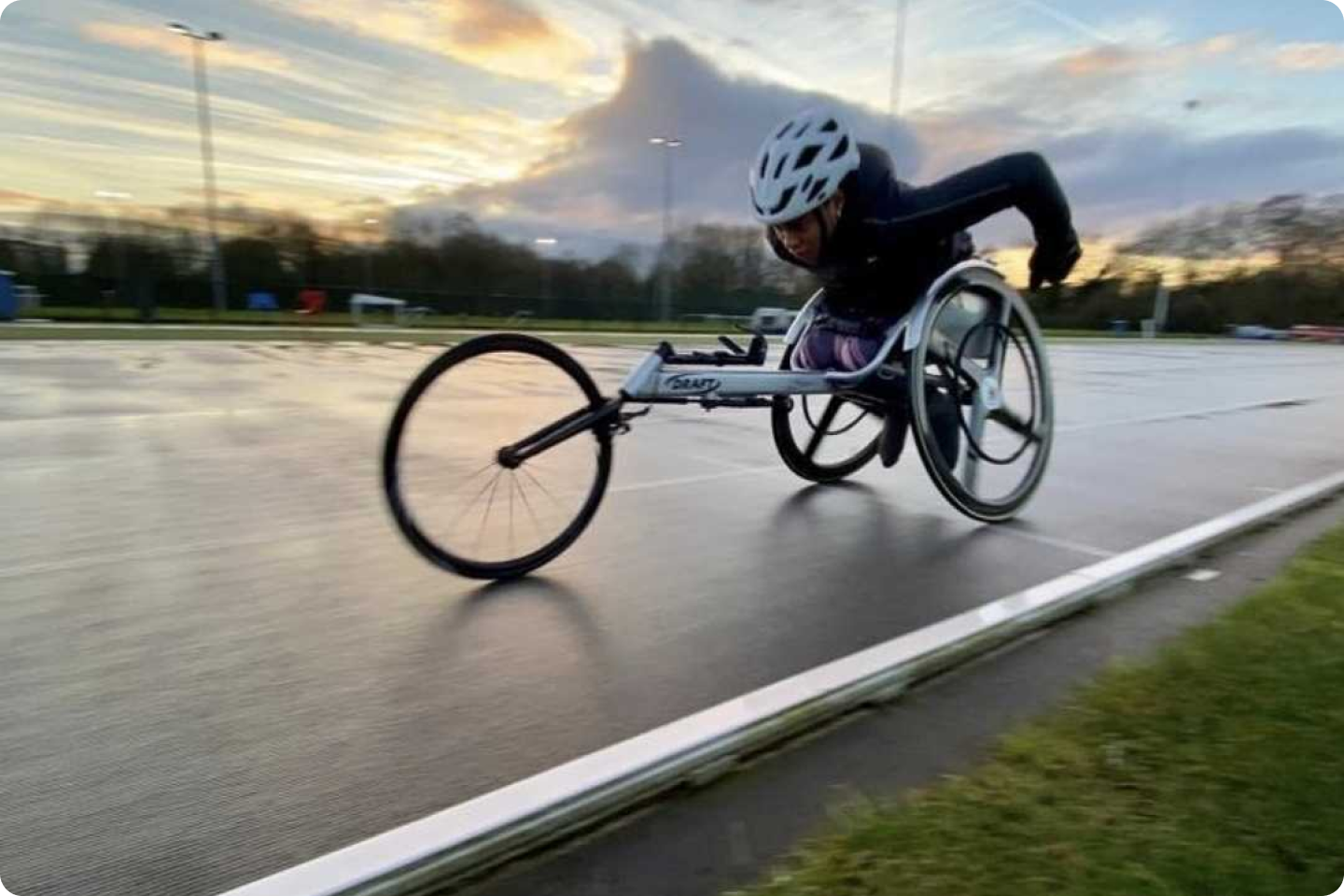 Photo of Karé Adenegan using a racing wheelchair moves swiftly down an outdoor track. T