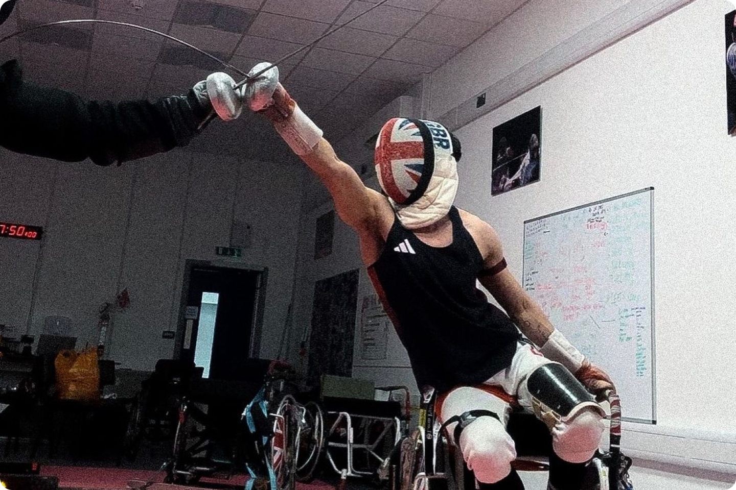 Photo of Oliver Lam Watson in his fencing gear and sat in a wheelchair