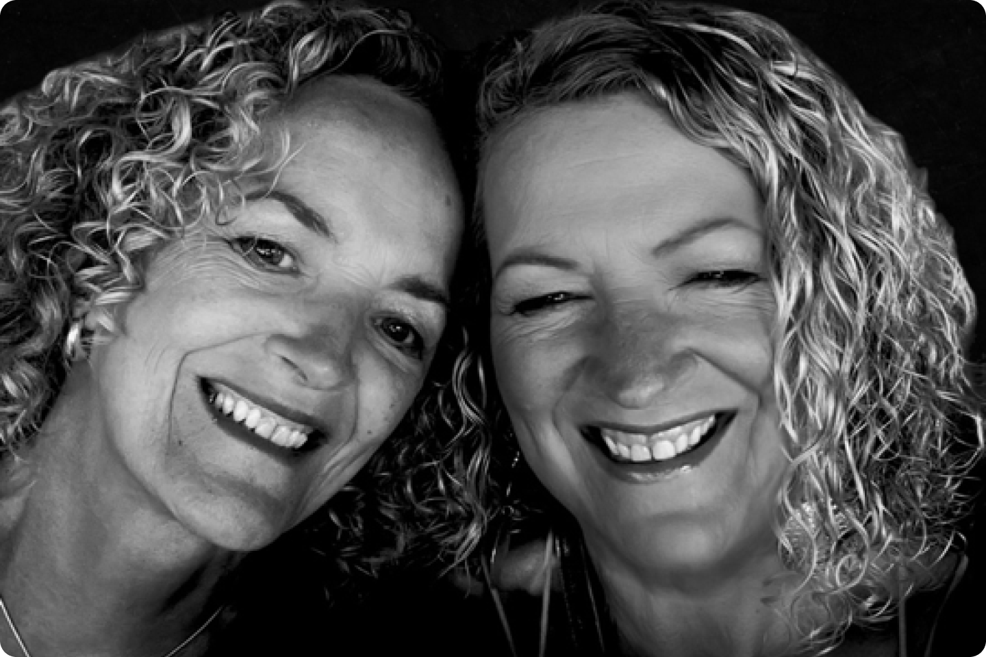 Black and white image of Julie Soroczyn and Mary Fickling - both women have curly shoulder length hair and are smiling.