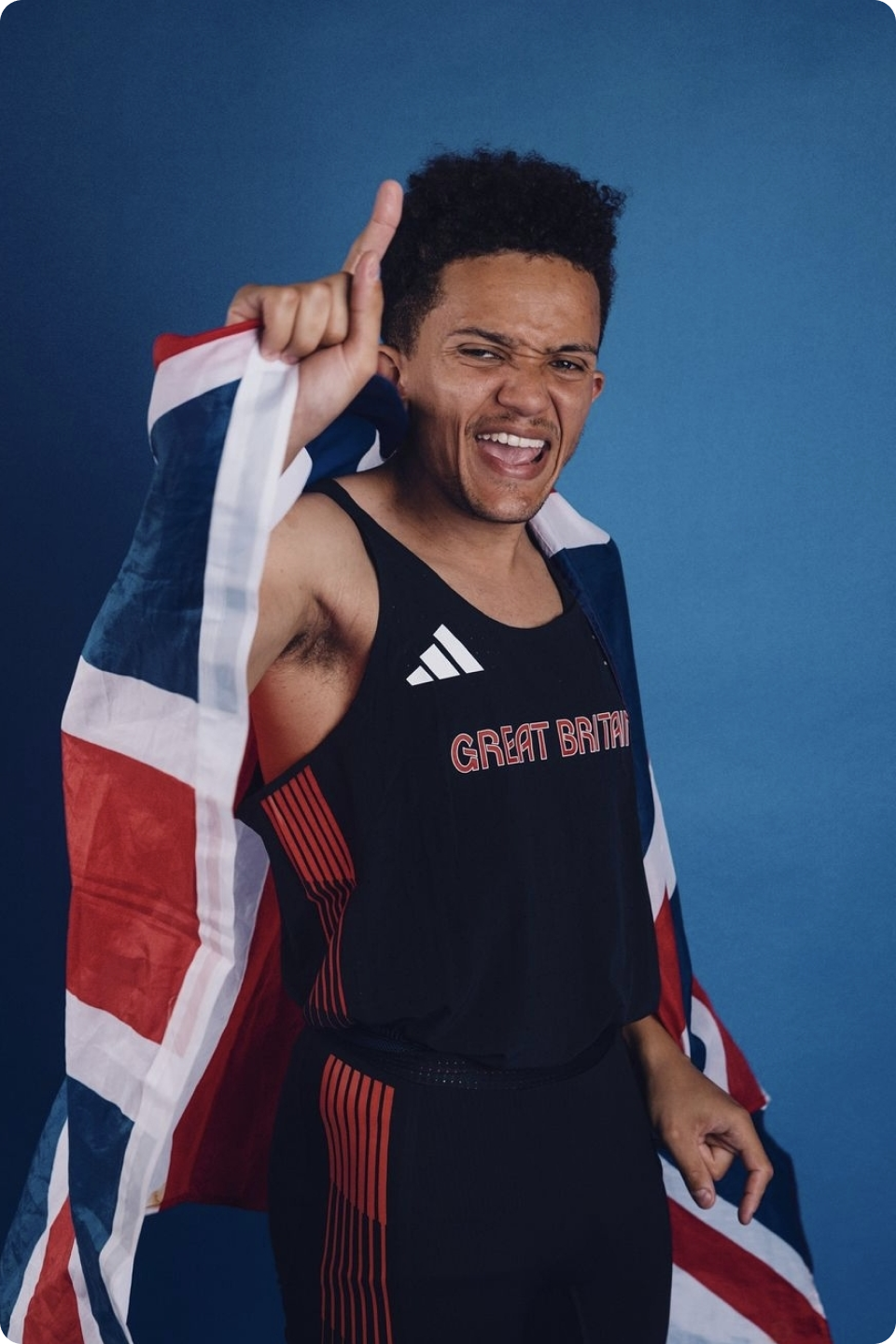 Photo of Thomas Young wearing his Great Britain sports clothing with the Union Jack flag wrapped around him - with one finger pointing up in the air