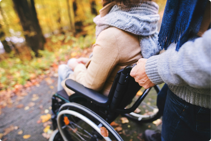 person pushing someone in a wheelchair, they are outside near lots of trees