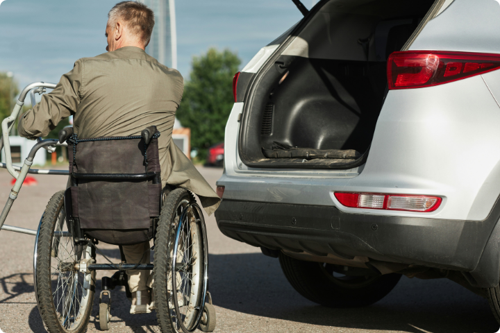 man in a wheelchair next to the open boot of his silver car