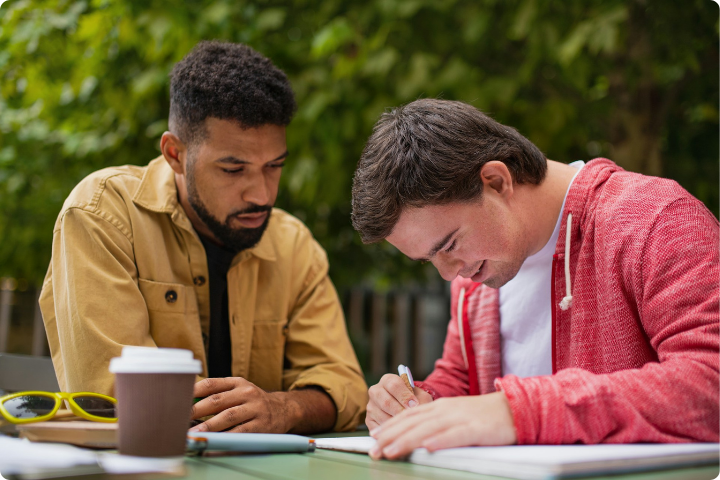 two men sat outside, one is completing some paperwork