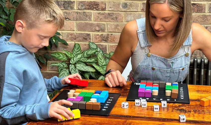 A woman and a young boy sit at a wooden table playing puzzles and games from the happy puzzle company