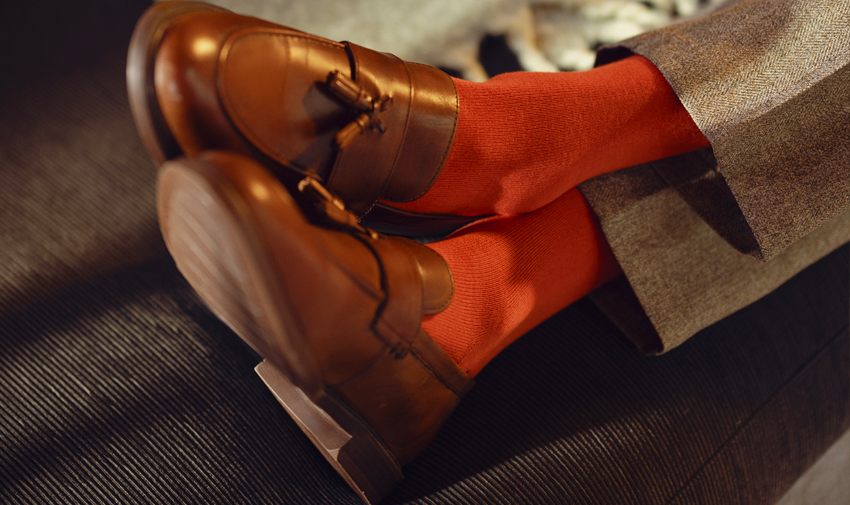 A pair of mens legs, wearing red socks and brown shoes relaxed with feet crossed