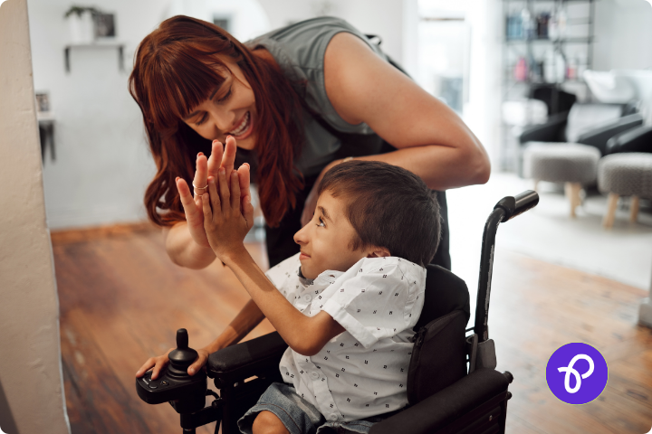 A mum with her disabled child, a young boy who is a wheelchair user are in the kitchen and are high fiving