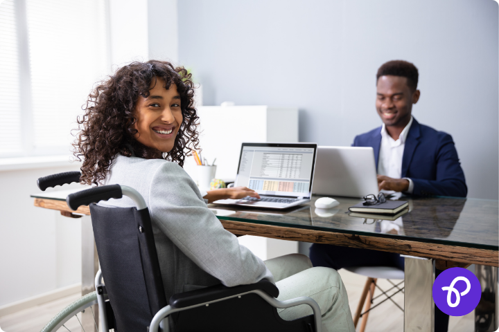 Woman using a wheelchair with brown skin and curly brown hair is sat at work on a laptop for a blog about the get Britain working white paper and how it affects disabled people