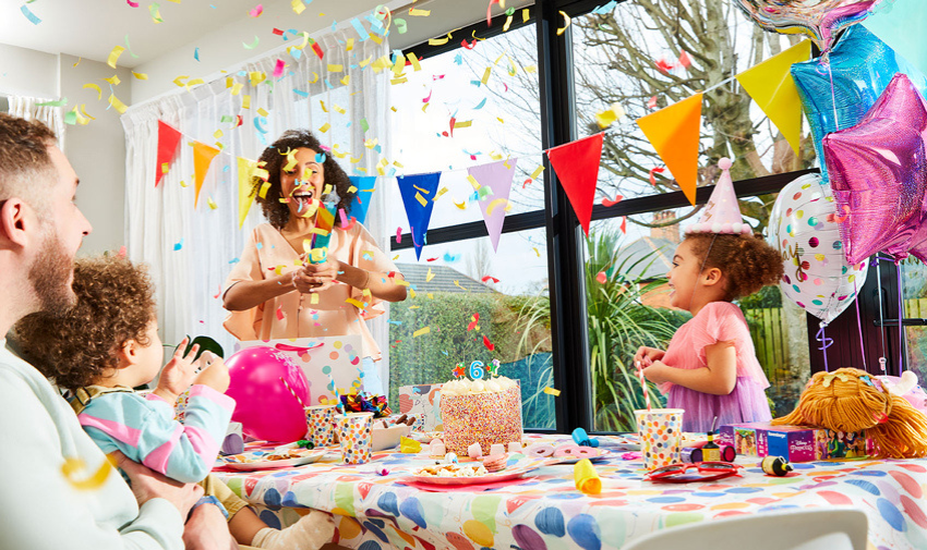 A children's family party scene, with kids and cake and banners and party poppers.