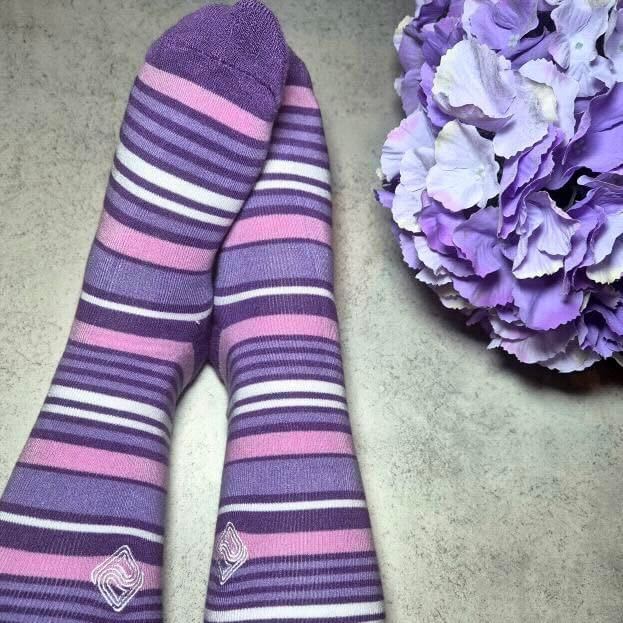 A pair of feet wearing purple stripy socks with a hydrangea blossom next to them celebrating Purple Sock Day for the International Day of Disabled People 