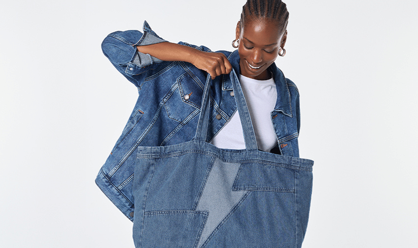 A black female model dressed in denim jacket and holding large denim tote bag