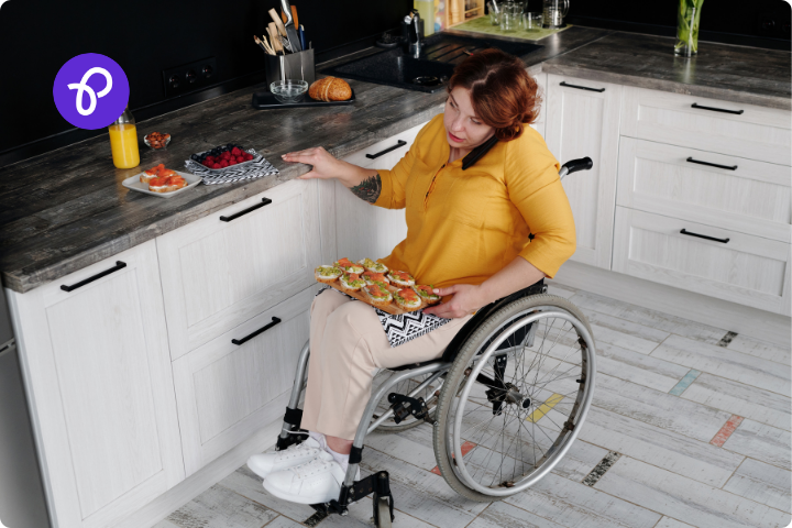 A disabled woman is cooking in a modern kitchen, she is wearing a yellow blouse, has short red hair and is a wheelchair user