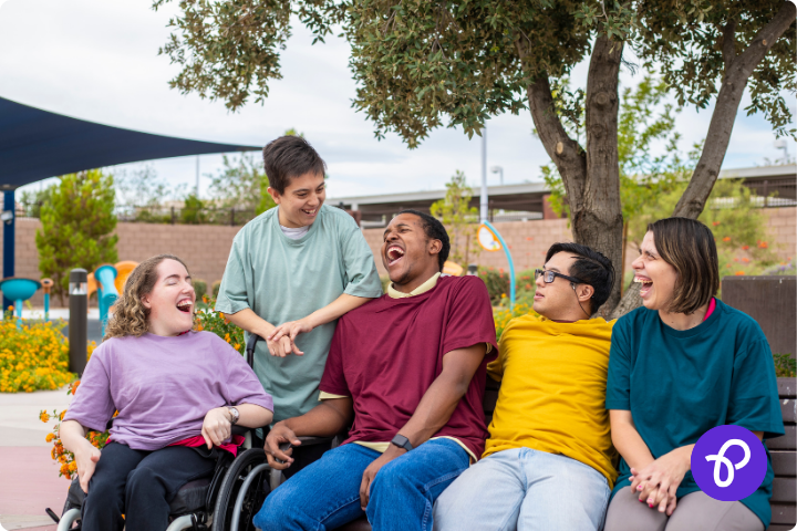 A group of five disabled people are sat outdoors, they are wearing brightly coloured t-shirts and are laughing