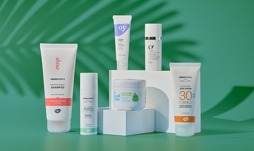 A range of beauty products from Green people on a green background, there is shampoo, SPF and other products in tubes and tubs that are white