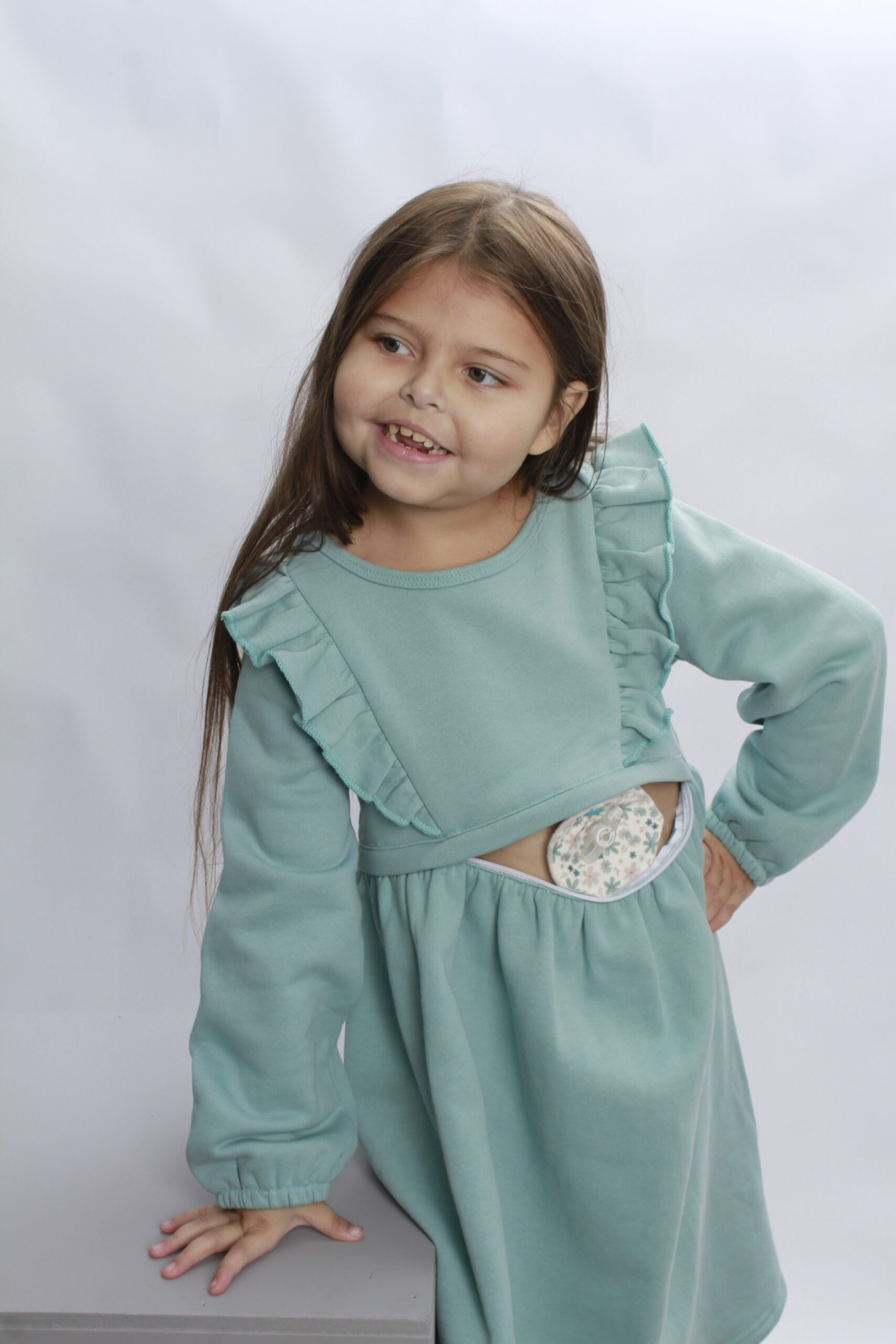 A young girl poses in a dress with a zip in the tummy to access a stoma bag, adaptive accessible clothing for disabled children in the UK