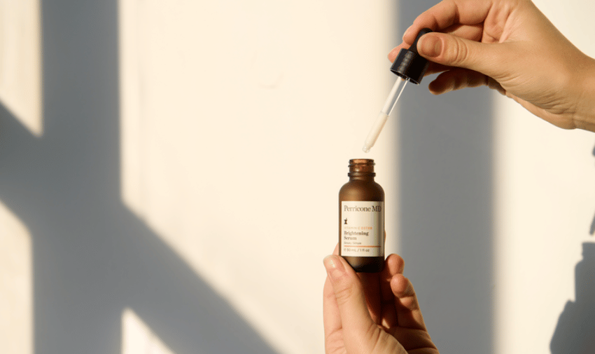 A bottle of perricone oil with a dropper and a hand holding both the bottle and the dropper lid