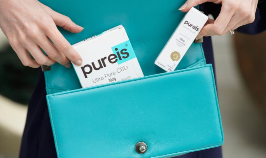 A close up on a woman's handbag with hands putting in two boxes with Pureis CBD on them