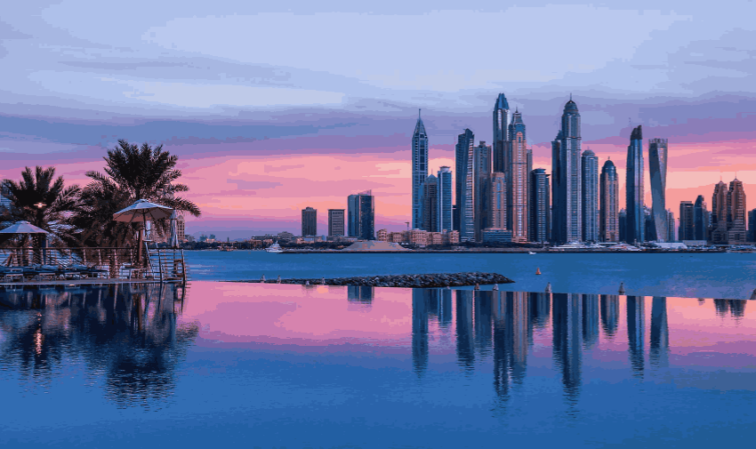 A skyline with palm tress and high rise buildings, the sky and water are blue and pink