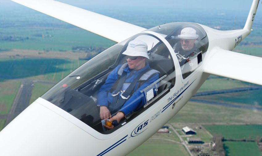 Two men are in a small light aircraft  flying over green fields