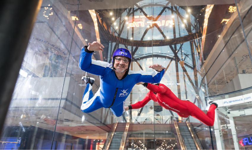 a man in a blue jumpsuit is doing an indoor sky dive with a person in a red jumpsuit guiding him at ifly indoor skydiving