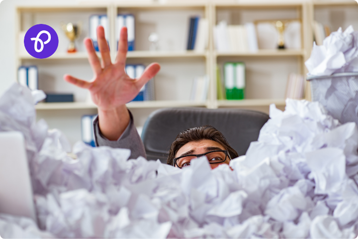 A man is drowning under a lot of paperwork, screwed up balls of paper cover his body and just his eyes and top of head is visible along with an outstretched arm