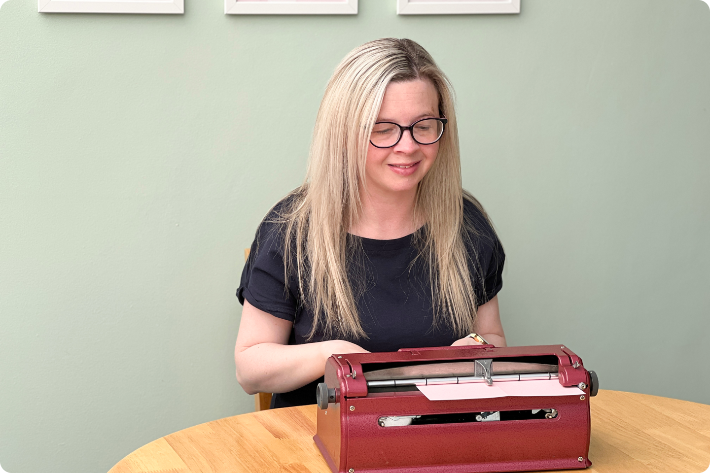 A white woman with long blonde hair is sat at a braille typewriter at a desk