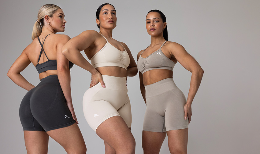 Three women are posing in activewear, shirts and crop tops in black white and beige, they look strong and powerful 