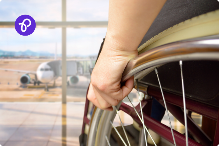 a closeup of a wheelchair users hand on a wheel at an airport looking out of a window towards a plane