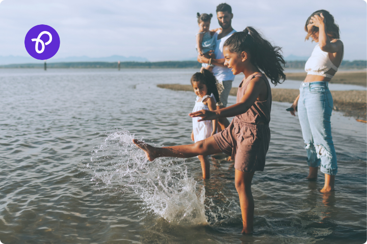 A family with a man, woman and three children are in the sea at the shore kicking and splashing