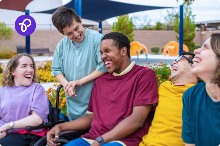 A group of disabled teenagers are laughing and joking together in a park outdoors