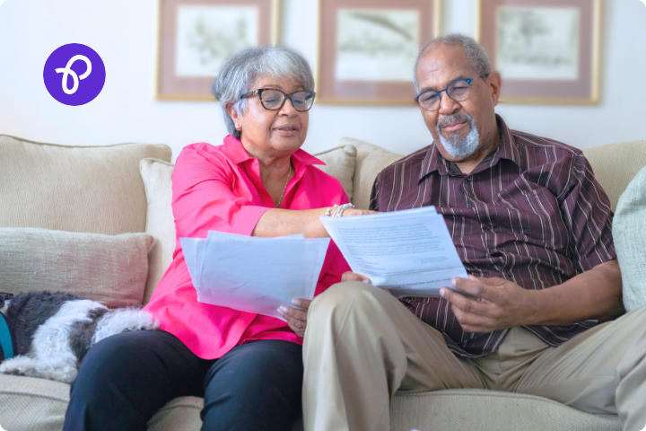 An older couple are sat on a sofa looking through paperwork in a living room