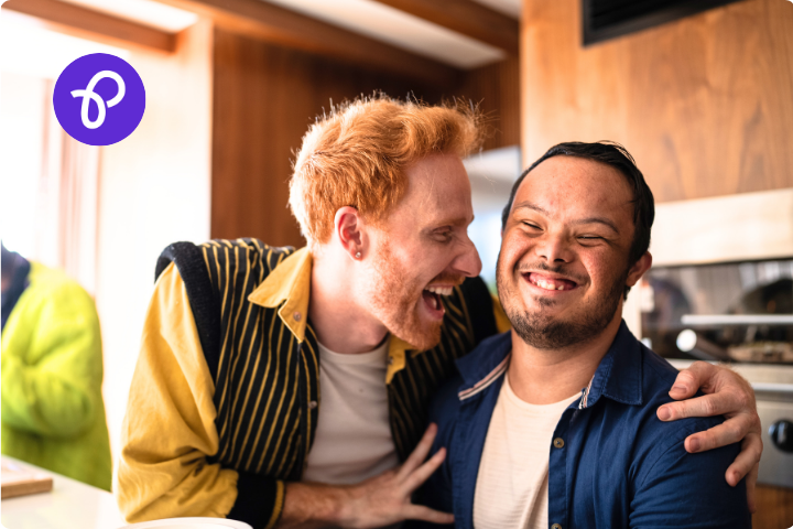 A man caring for a disabled man, they are laughing and indoors