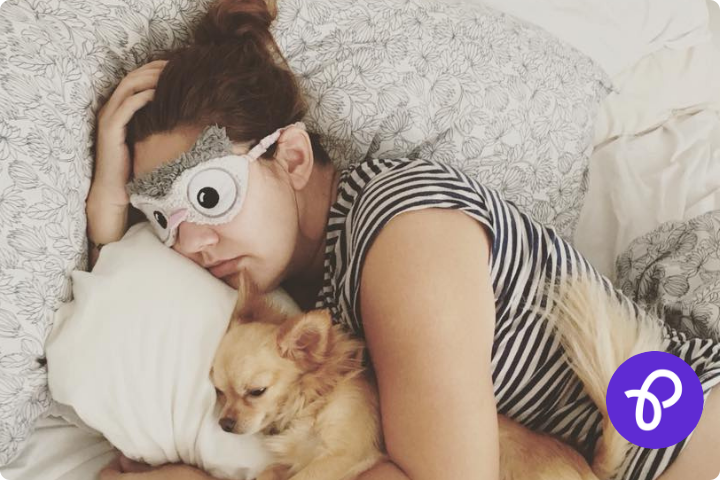 Woman sleeping in a bed with an eye mask on hugging a dog