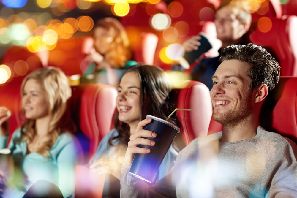 A group of friends enjoying a movie night with drinks and popcorn in a cinema. Purpl offers accessible savings on cinema tickets for disabled people across the UK.