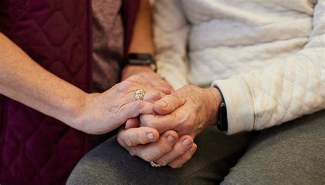 An old couple holding hands supportively, following announcements to disability benefits changes in the UK