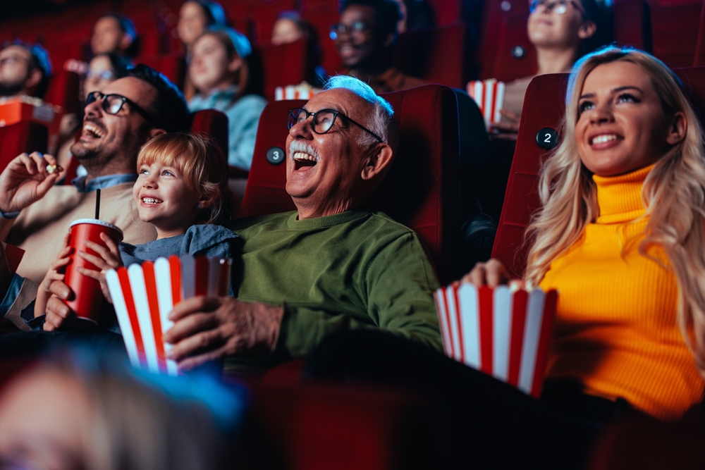 A family of all ages laughing and enjoying popcorn in a packed cinema. Purpl members, including disabled people, can save up to 40% on tickets at major cinemas like ODEON, Vue, and Showcase.