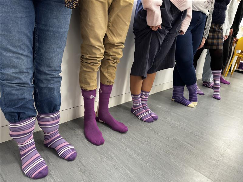 A row of people lined up wearing purple striped socks for Purple Sock Day, supporting disability and long term health condition awareness and highlighting inclusion within the Purpl discounts community.