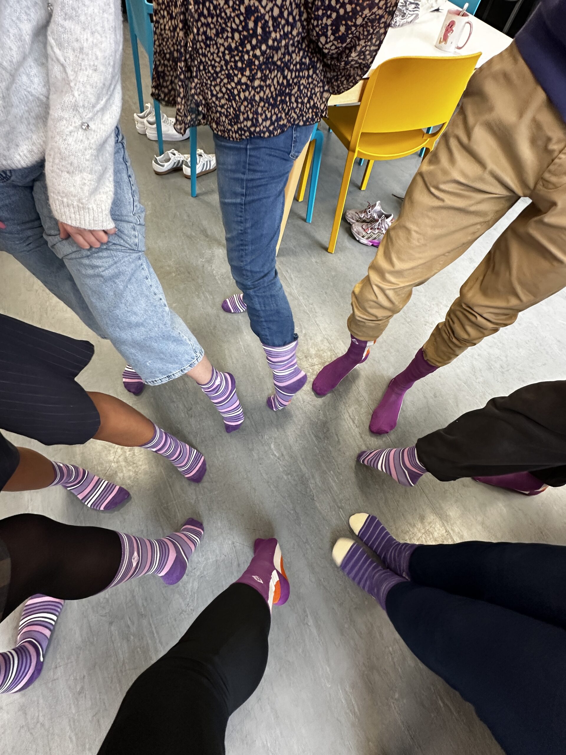 A group of people standing in a circle showing their purple striped socks for Purple Sock Day, raising awareness of disabilities and long term health conditions and celebrating the inclusive Purpl discounts community.