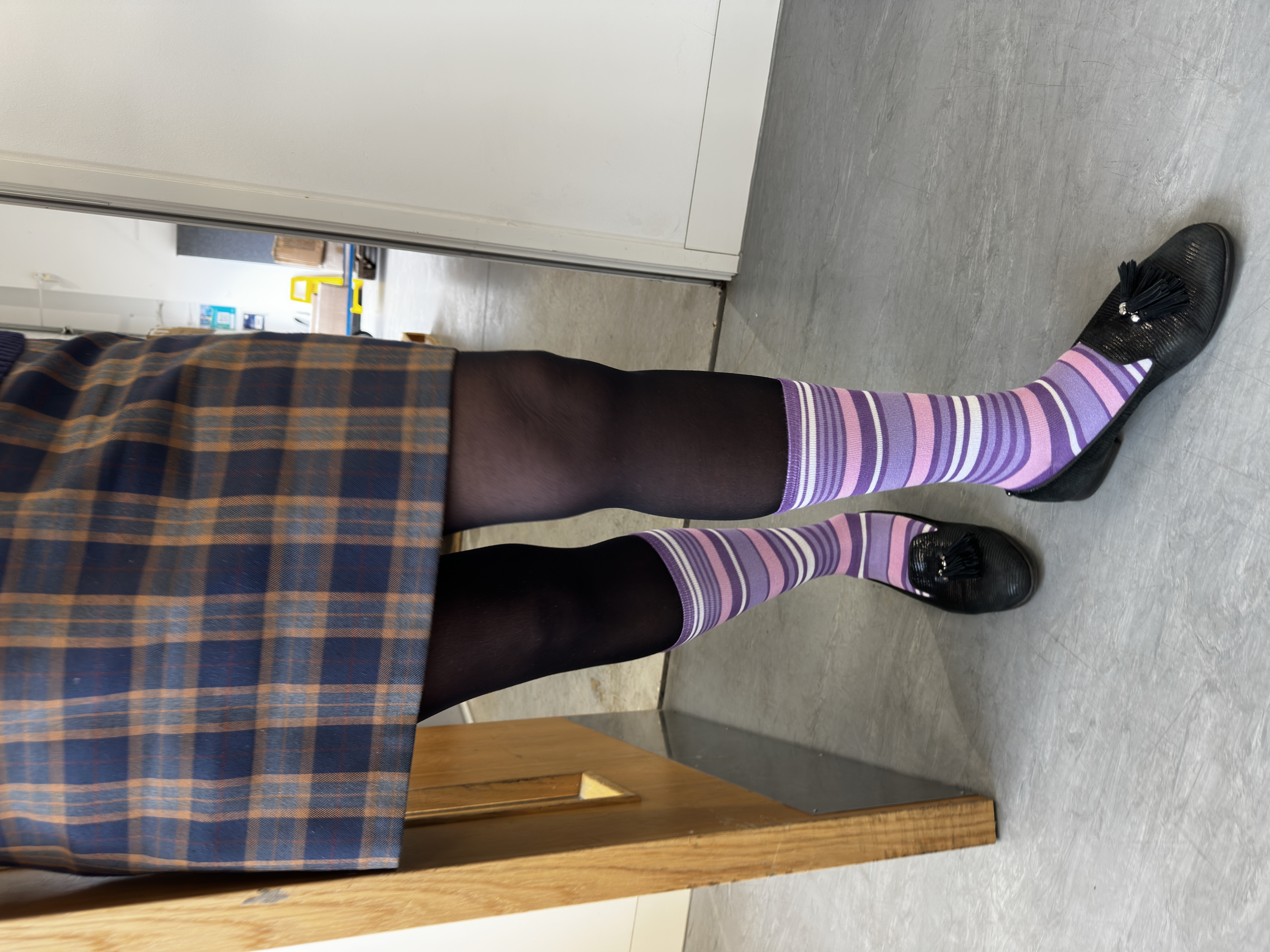 A person standing in a doorway purple striped socks for Purple Sock Day, supporting awareness of disabilities and long term health conditions while championing the Purpl discounts community.