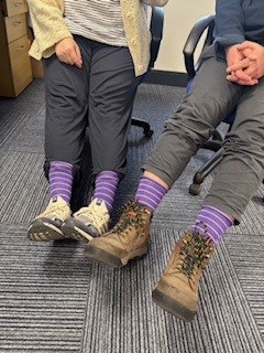Close-up of two people wearing purple striped socks for Purple Sock Day, raising awareness of disabilities and long-term health conditions while celebrating inclusion and Purpl discounts.