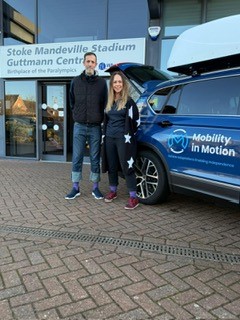 People standing outside Stoke Mandeville Stadium next to a Mobility in Motion vehicle wearing purple socks for Purple Sock Day, supporting disability awareness and long-term health conditions while promoting Purpl discounts and inclusive savings.