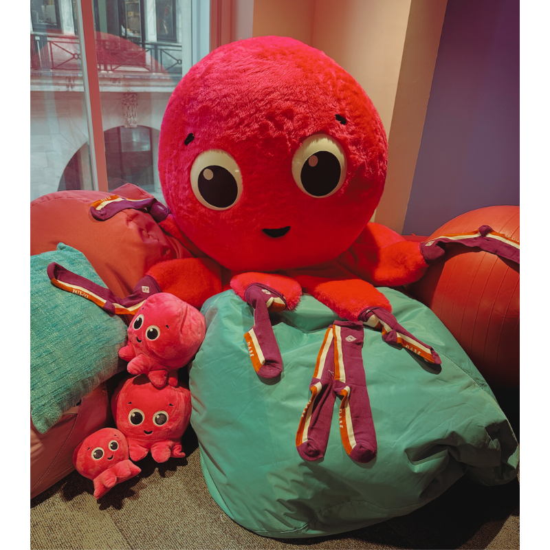 Large red plush octopus displayed with purple socks draped over its tentacles, shown as part of Purple Sock Day to raise awareness of disabilities and long-term health conditions, with links to accessibility, inclusion and Purpl discounts.